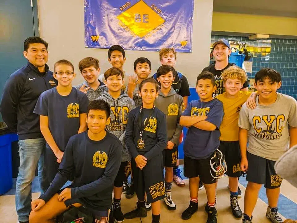 Group of boys posing indoors in matching gray shirts, smiling in front of a banner.