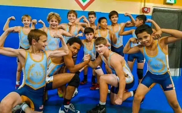 Youth wrestling team posing in blue singlets and socks, flexing in a gymnasium