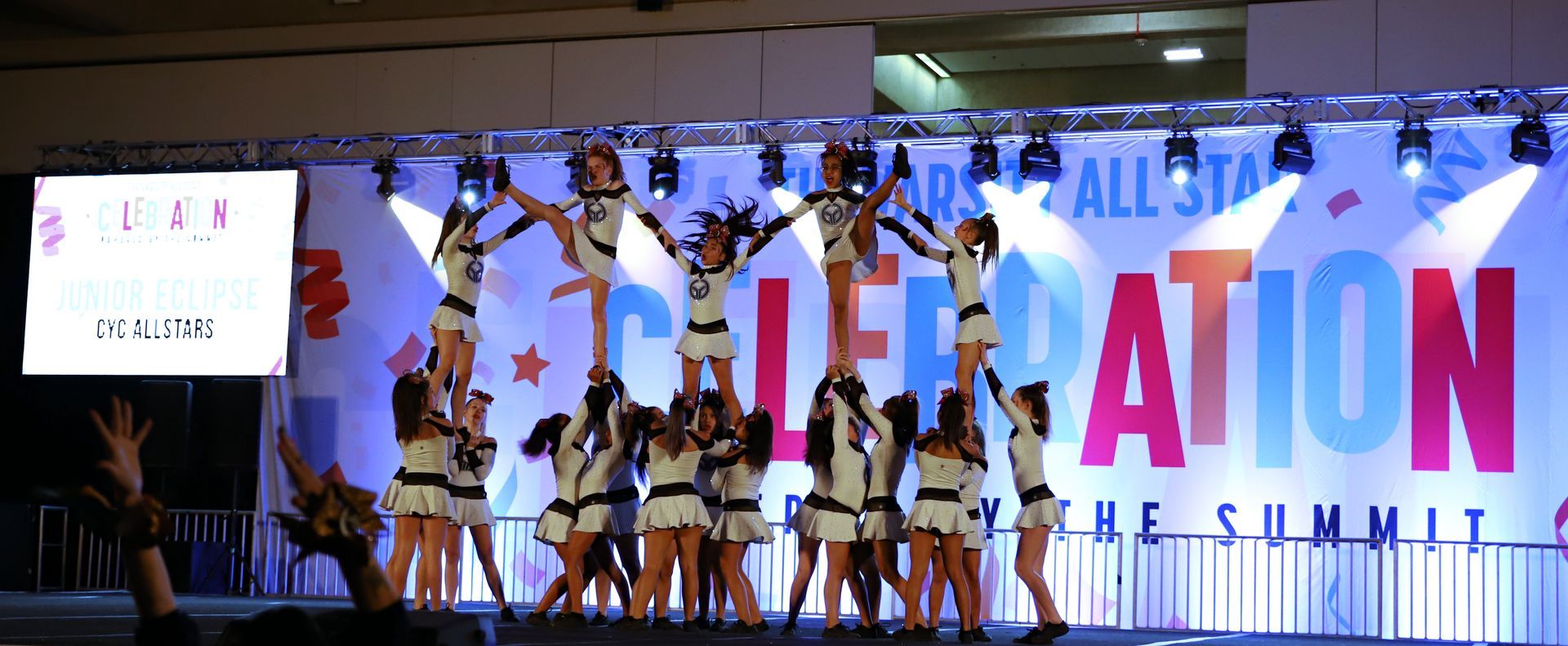 Cheerleaders performing a pyramid stunt on a lit stage with a summit event banner