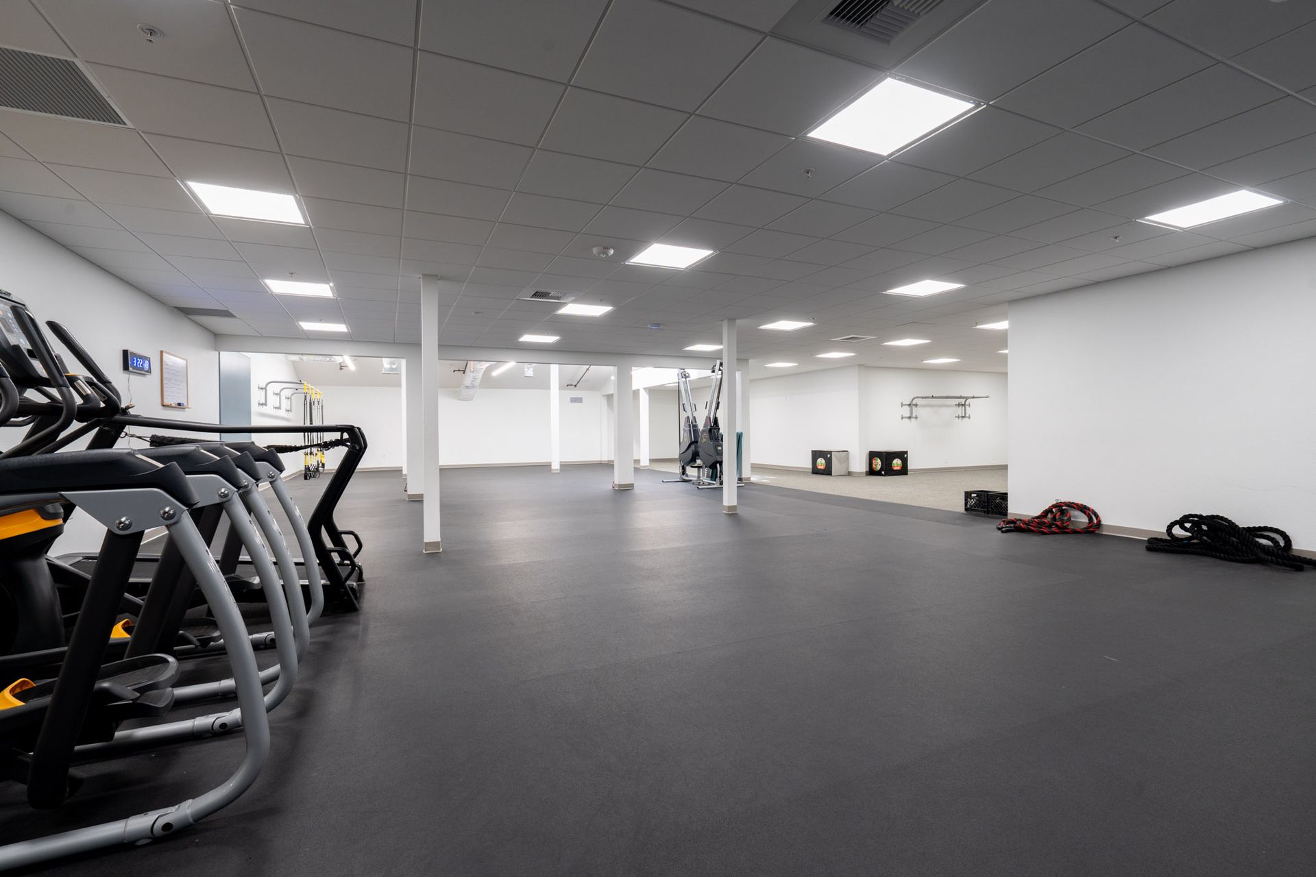 Empty gym with treadmills, dark flooring, and white walls under bright ceiling lights