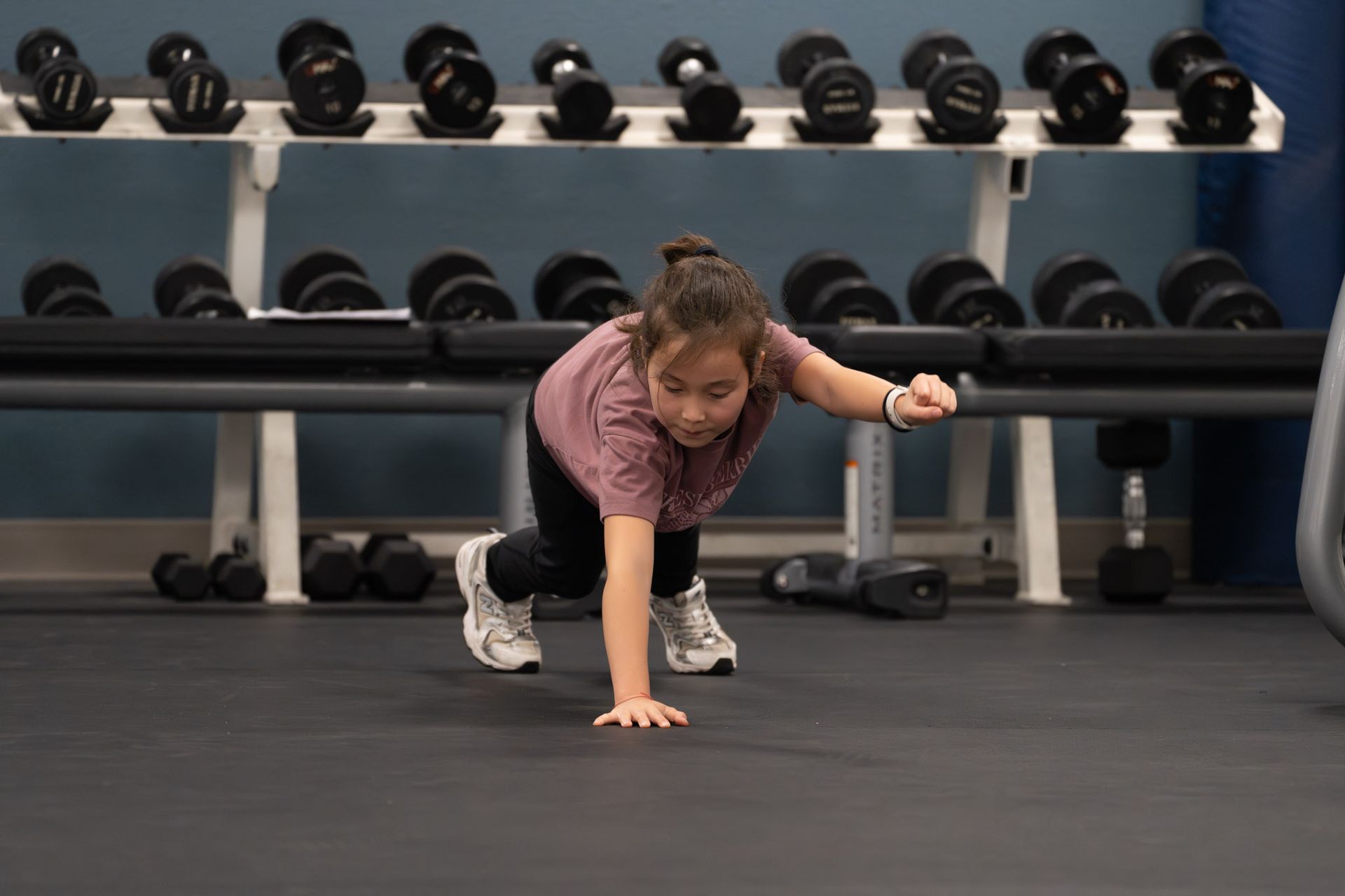 Person doing a one-arm balance stretch in a gym with dumbbells in the background
