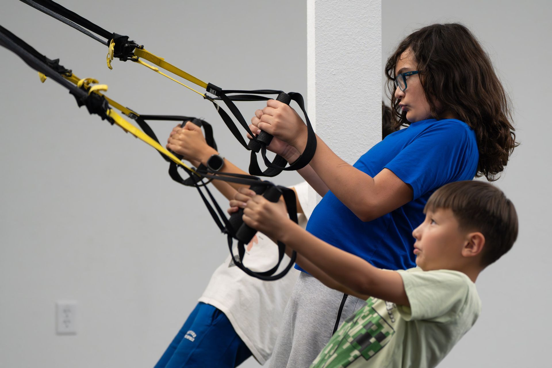 Two people using suspension straps in a gym, leaning back and pulling handles with focused expressions