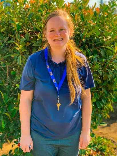 Smiling person in a blue shirt with a lanyard standing in front of green bushes