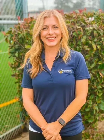 Woman in navy polo shirt smiling outdoors by a fence and greenery
