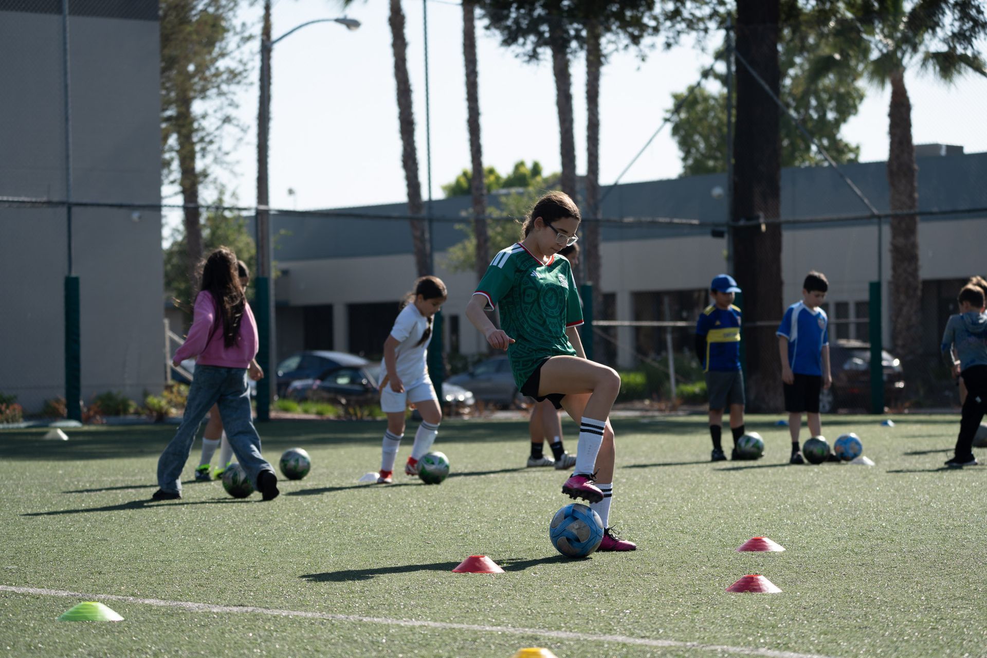 Children practicing soccer drills on a sunny field with cones and balls.