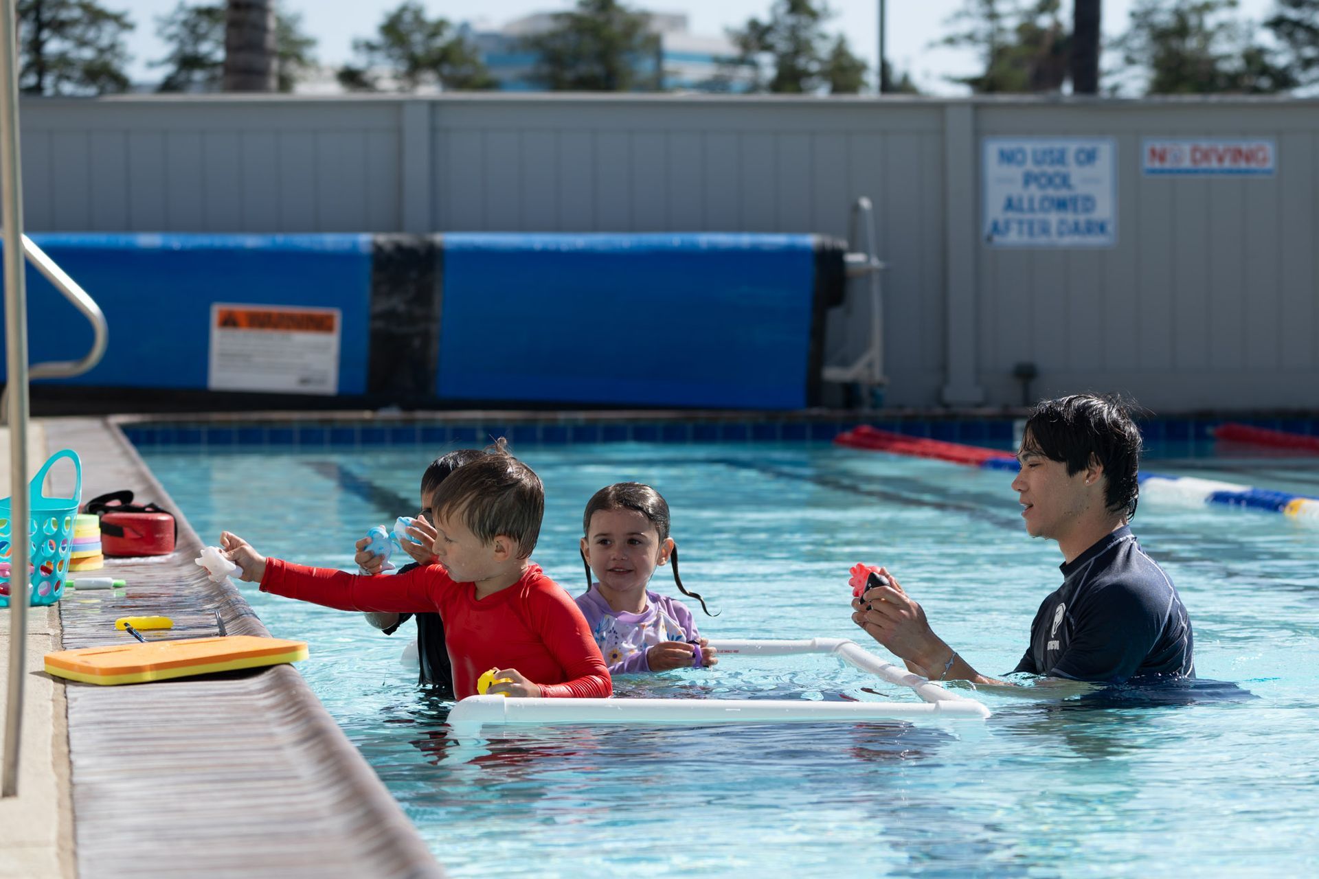 Three swimmers in an outdoor pool reach toward a poolside ladder