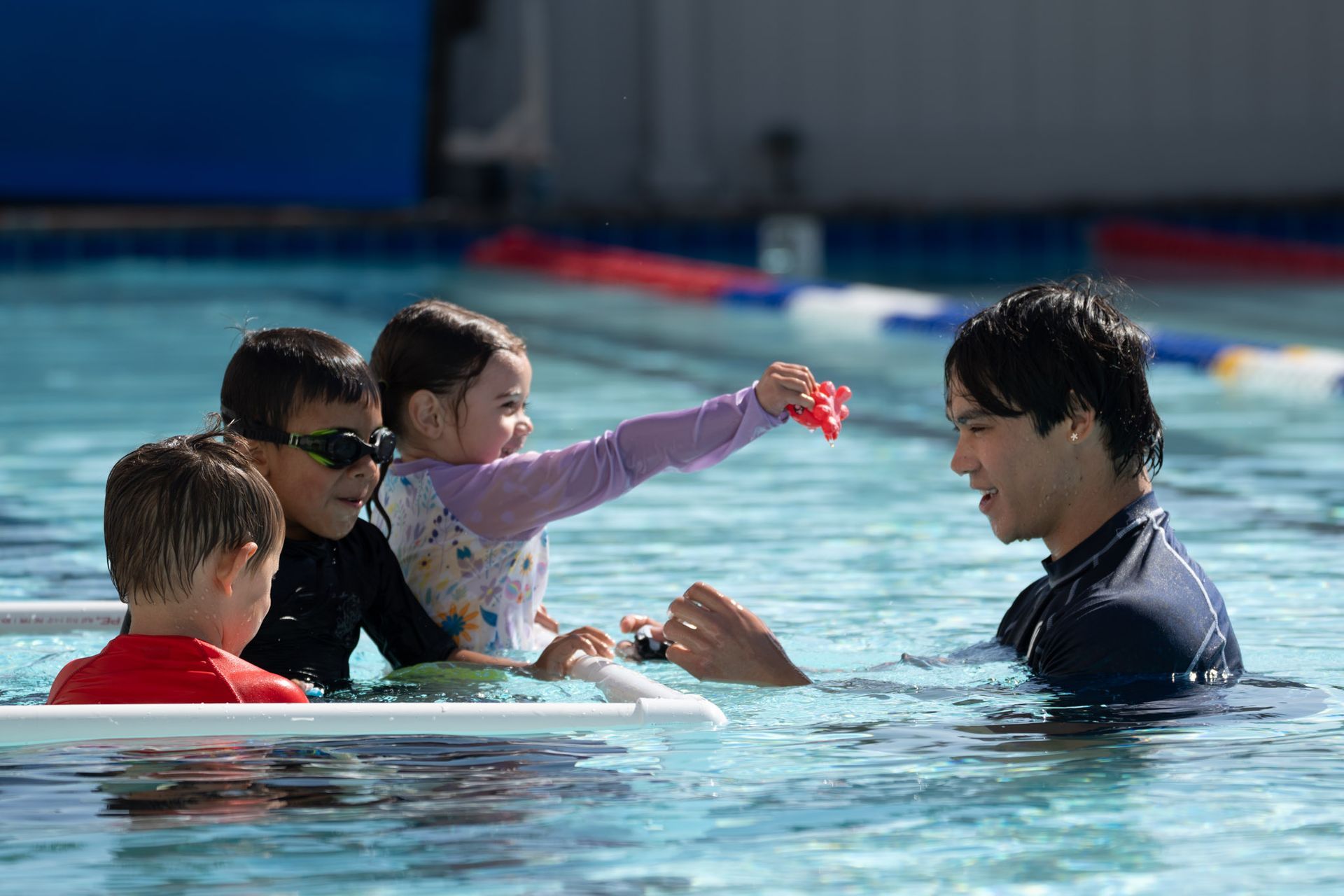 Children and an instructor in a swimming pool, reaching toward each other during a lesson