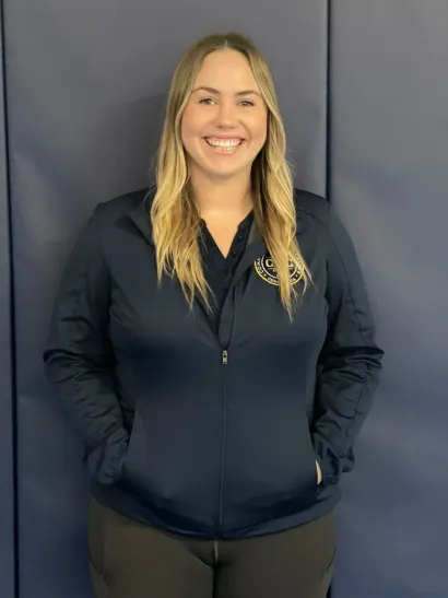 Smiling woman in a navy jacket standing against a dark backdrop