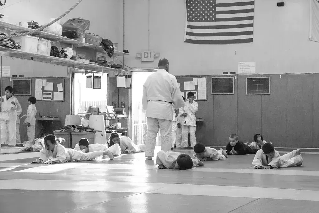 People practicing martial arts on mats in a dojo with a large American flag on the wall.