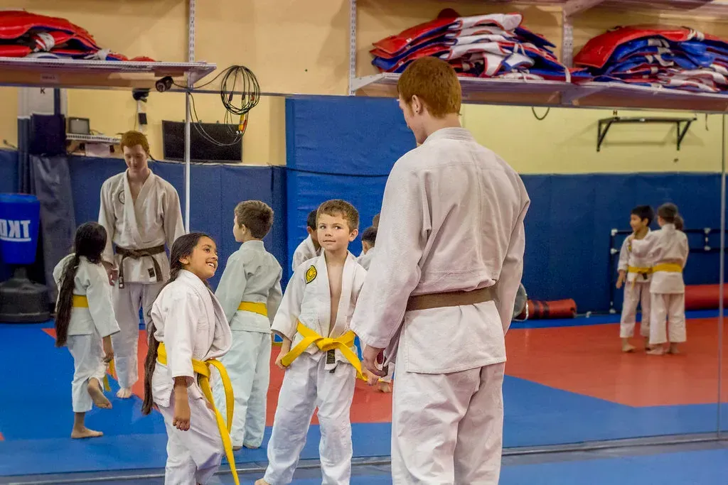 Martial arts class with children in white gis and yellow belts listening to an instructor in a gymnasium