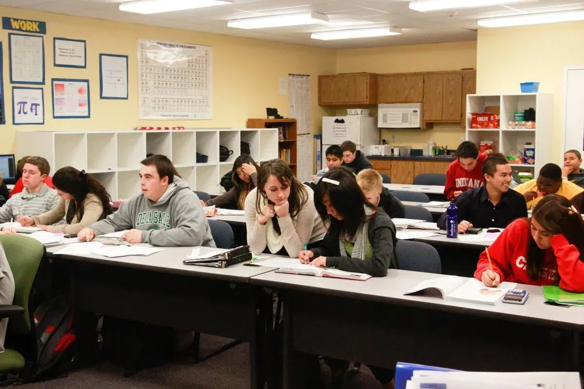 Students seated at tables in a classroom, writing on papers during a lesson.