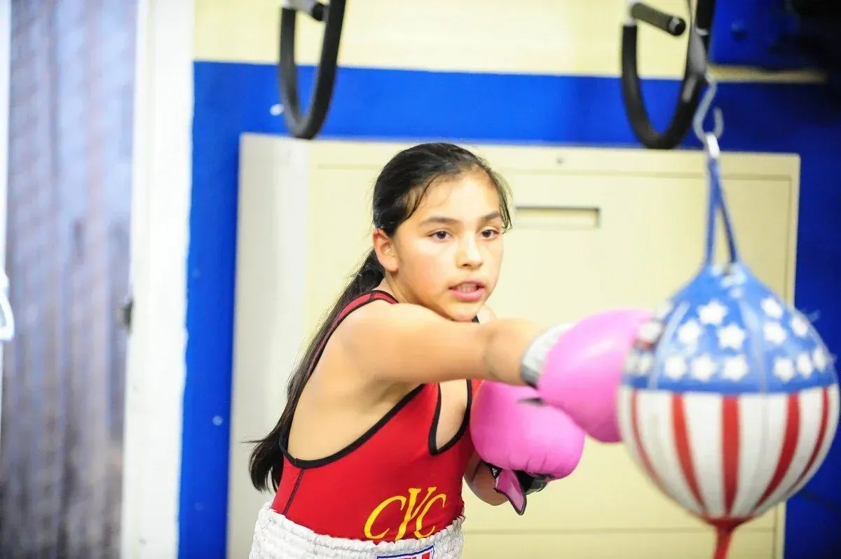 Boxer in red gear throws a punch at a striped training bag in a gym