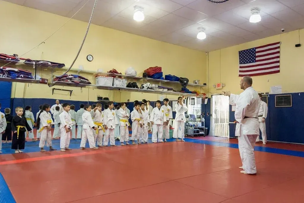 Martial arts class lined up in a dojo with a red mat and American flag on the wall