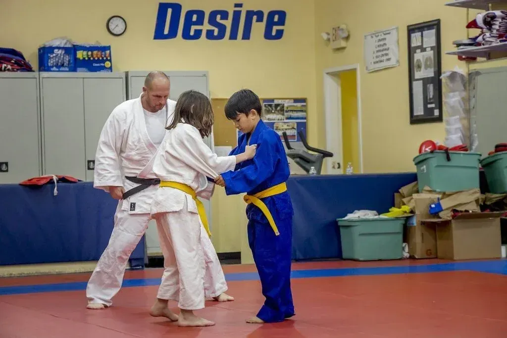 Two people in blue and white martial arts uniforms practicing grappling in a dojo