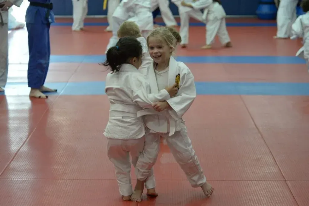 Two children in white judo uniforms practicing a hold on a mat in a dojo