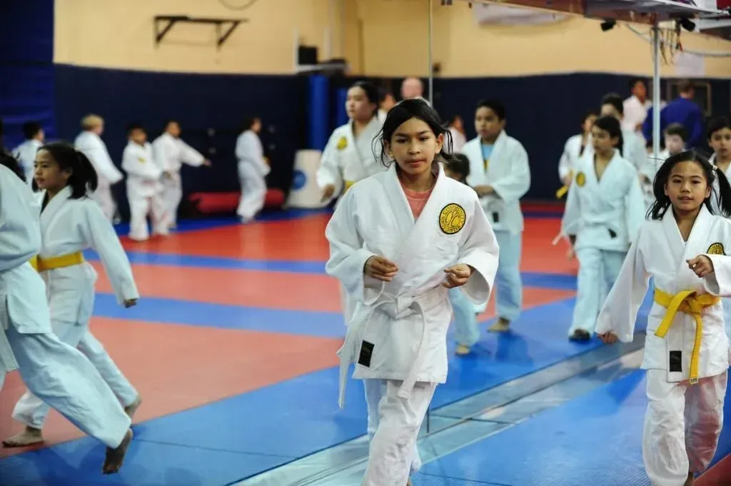 Students in white uniforms practicing martial arts on blue and red mats in a dojo