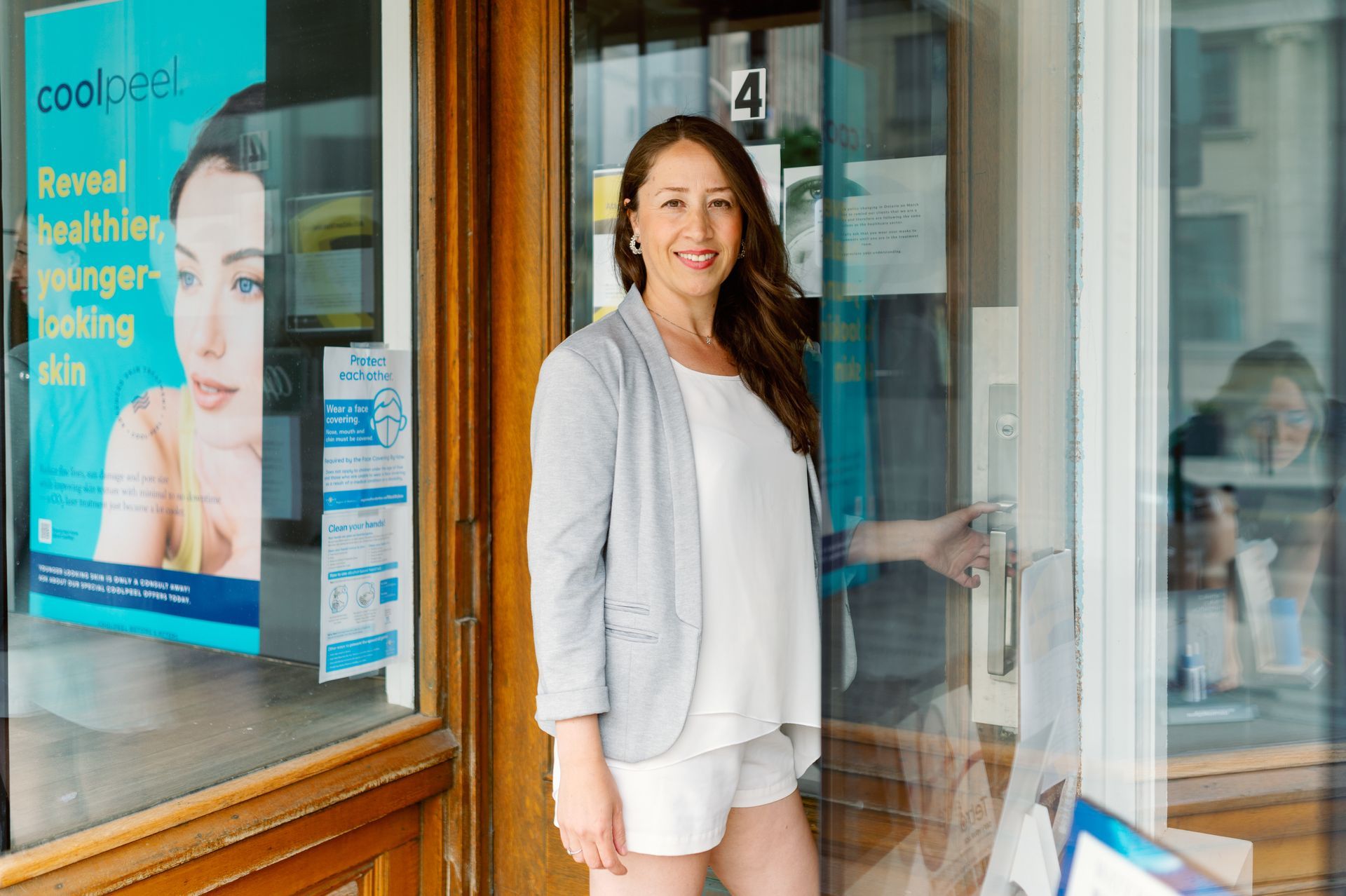 Woman in a white blazer standing in a shop doorway, smiling at the entrance.
