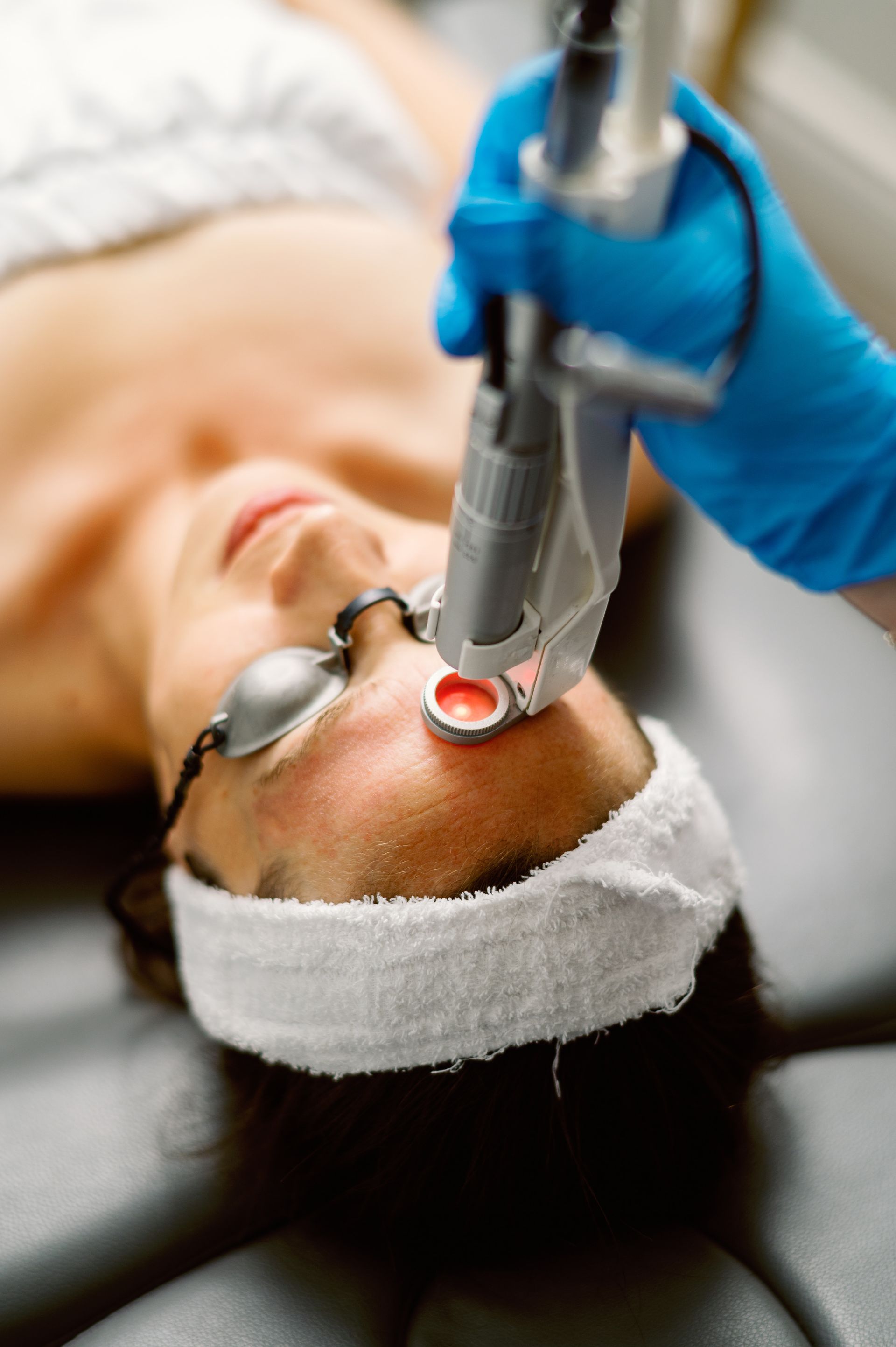 Aesthetic facial laser treatment on a reclining patient, with a gloved clinician holding the device to the face