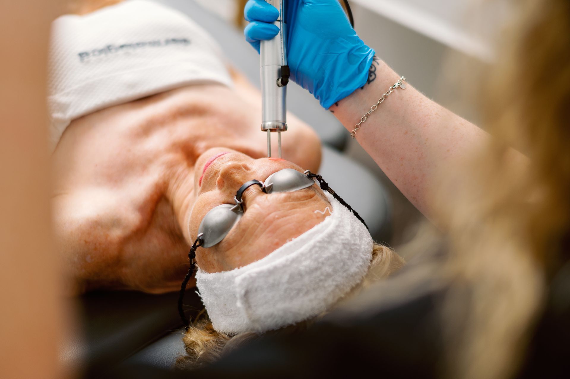 Medical procedure close-up with gloved hands using a syringe near a patient’s face under a surgical drape