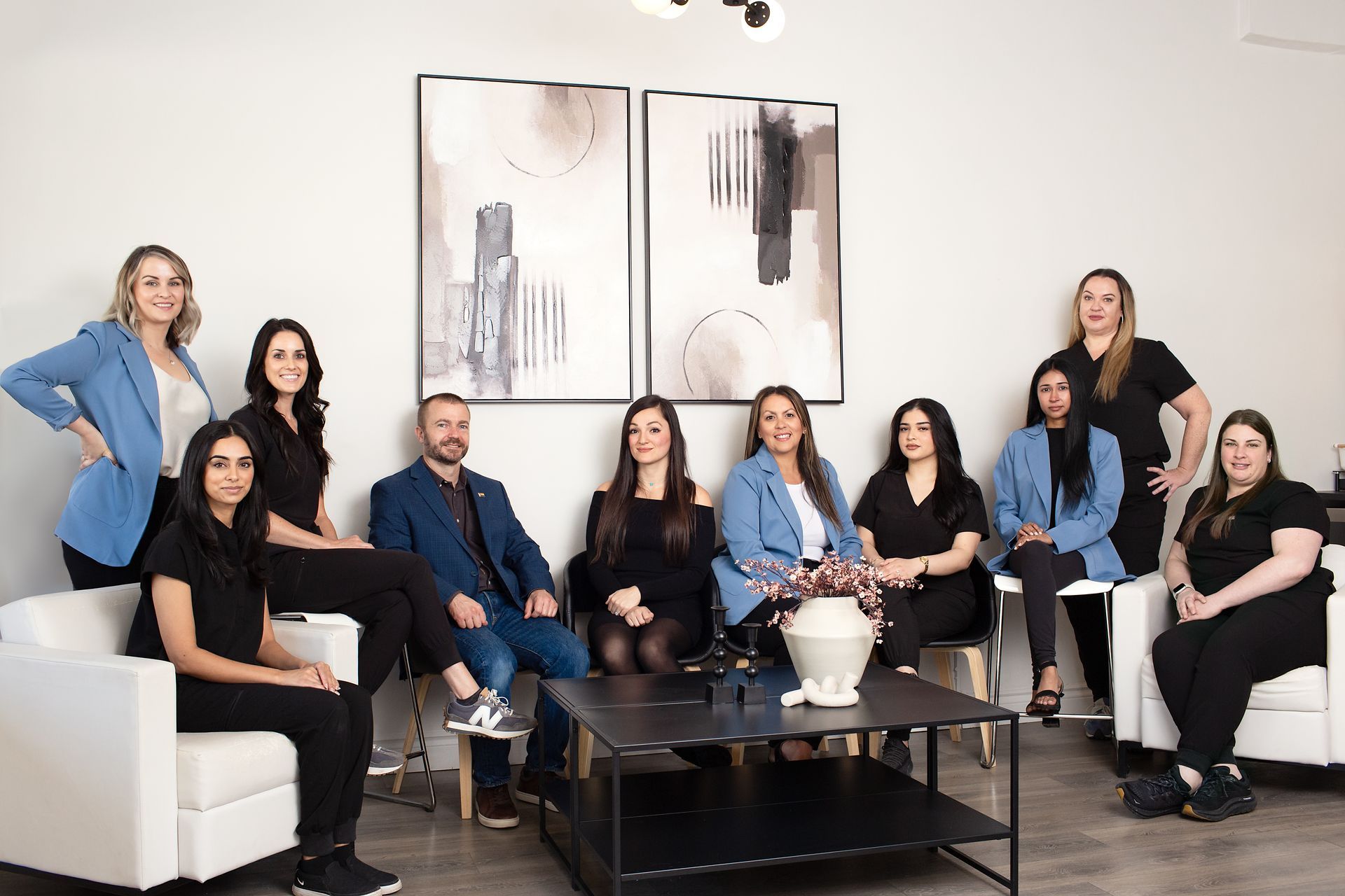 Group of people posing in a modern office lounge with white seating, black coffee table, and wall art.