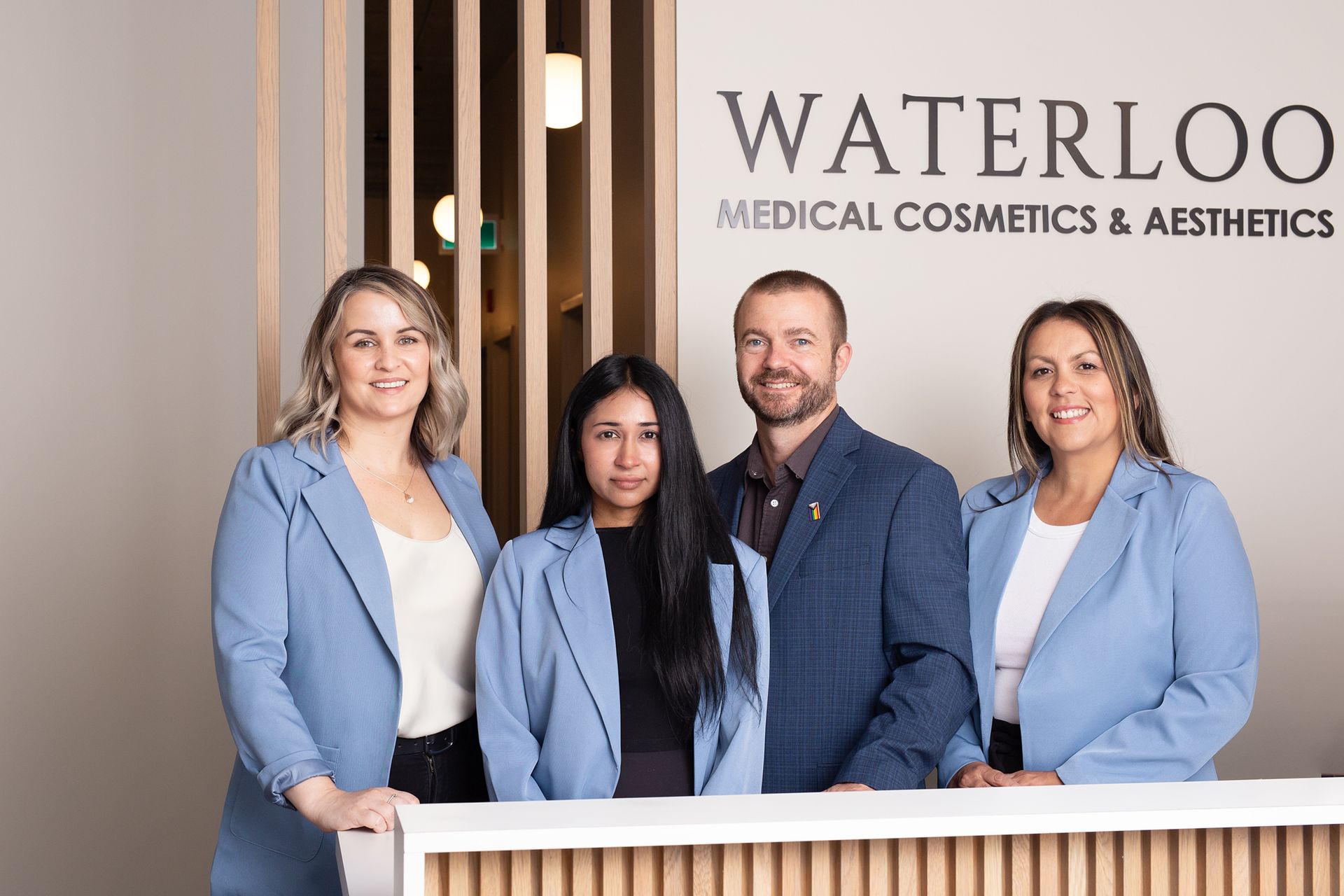 Four staff members in light blue blazers stand behind a reception desk at Waterloo Medical Cosmetics & Aesthetics.