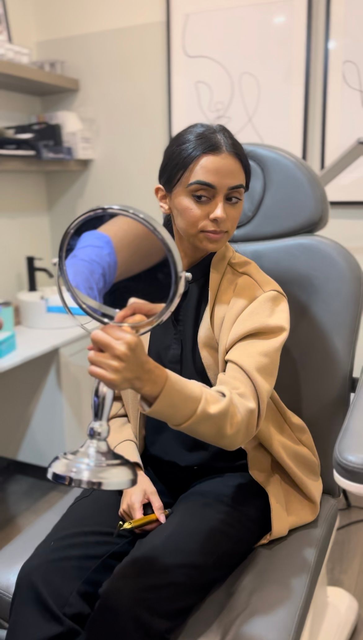A woman is sitting in a chair looking at herself in a mirror.