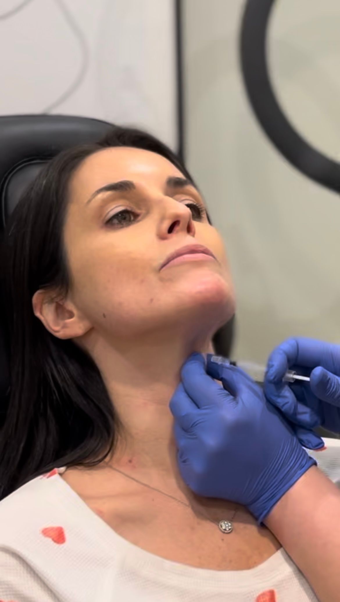 Gloved hands adjusting a neck area during a cosmetic procedure on a reclining woman