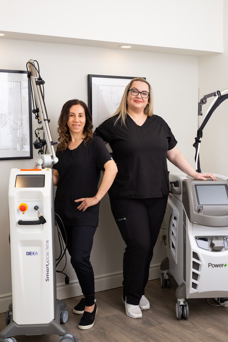 Two women standing beside medical laser equipment in a clinic room
