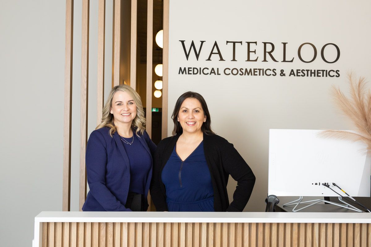 Two women at a reception desk in a Waterloo Medical Cosmetics & Aesthetics clinic lobby