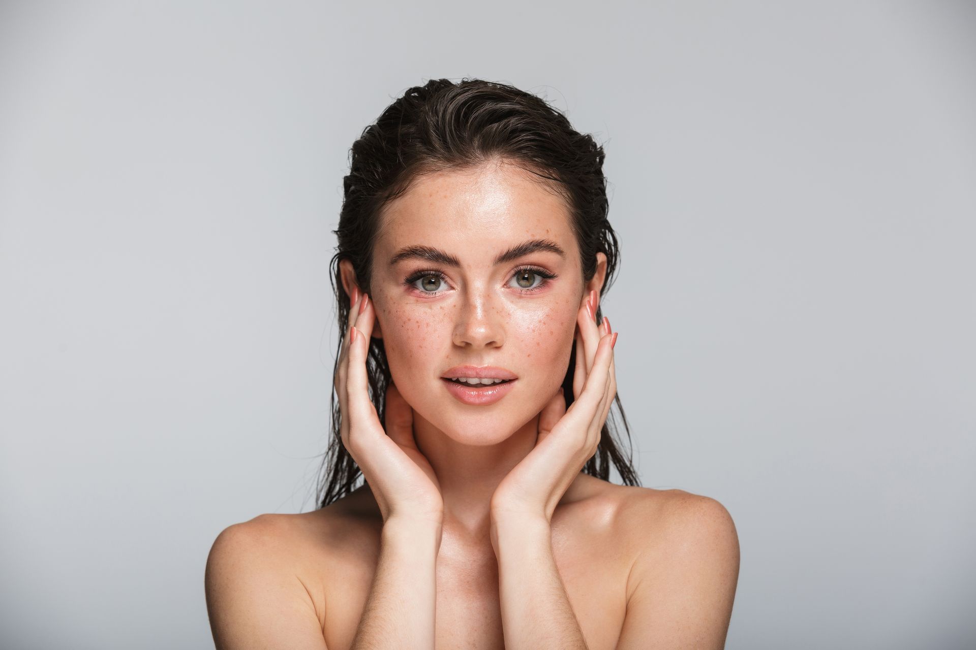 Portrait of a woman with hands on her cheeks against a gray background
