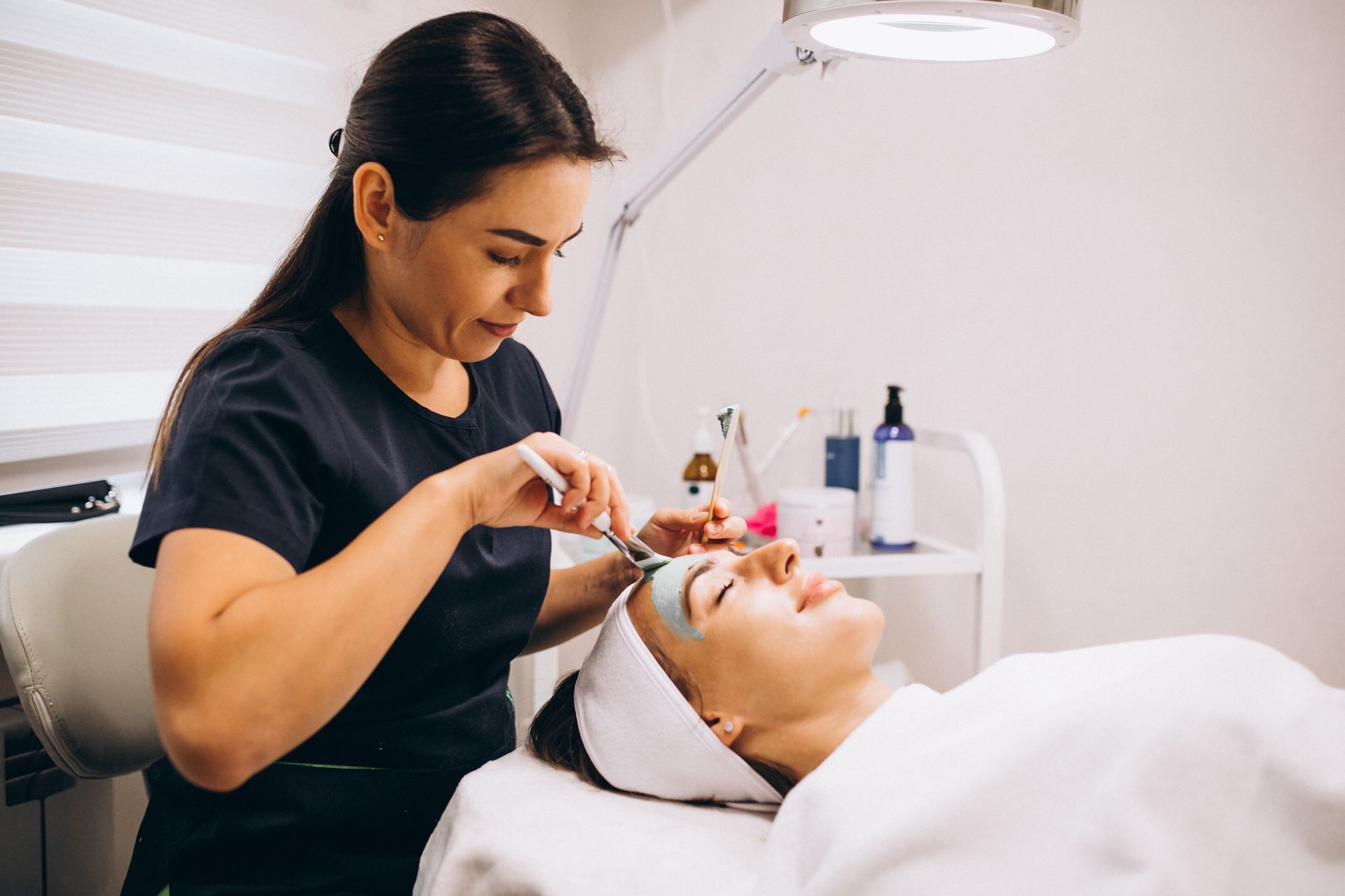 A woman is applying a mask to a woman 's face in a beauty salon.