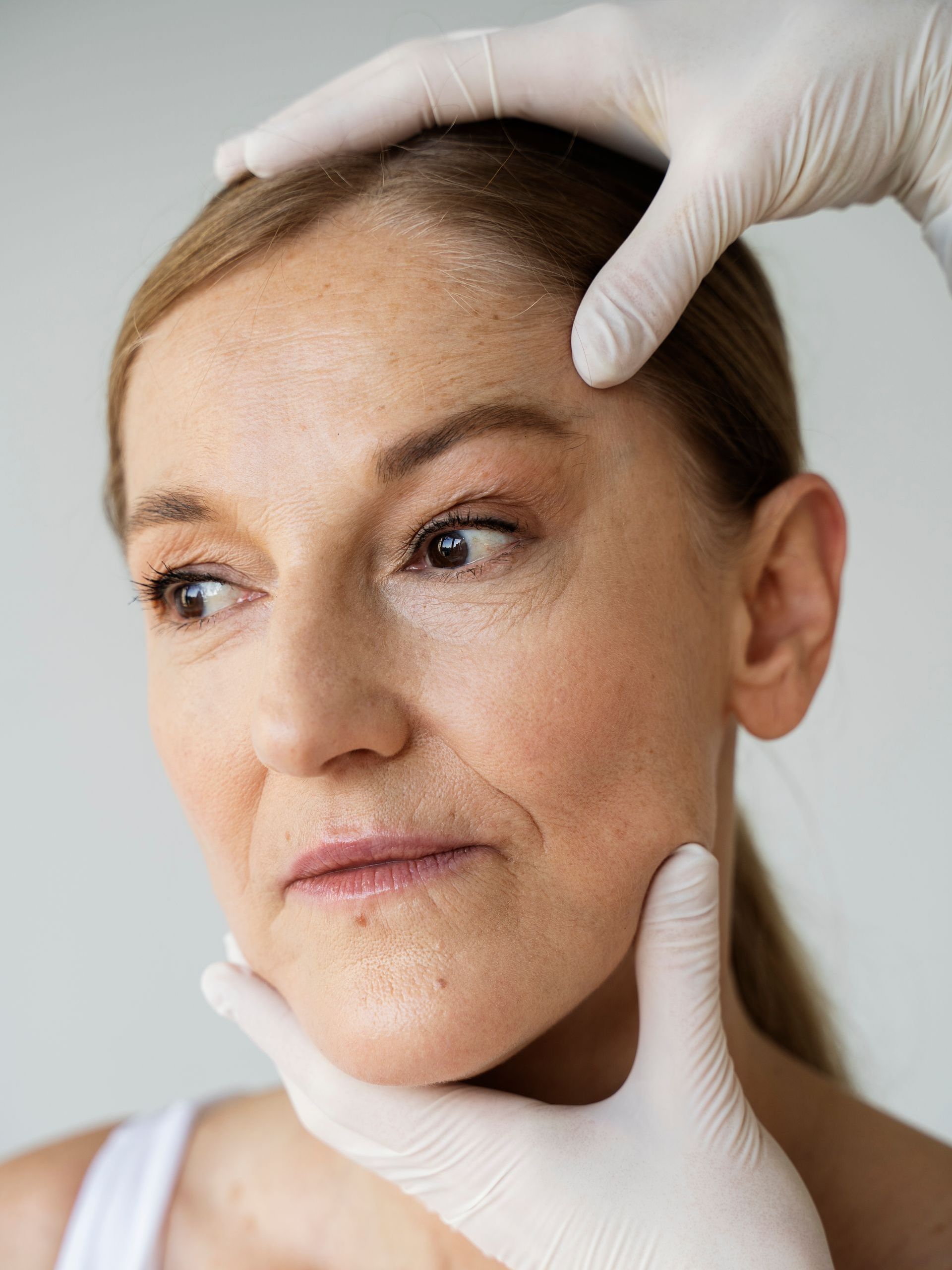 Gloved hands gently examine a woman’s face, suggesting a skincare or cosmetic consultation