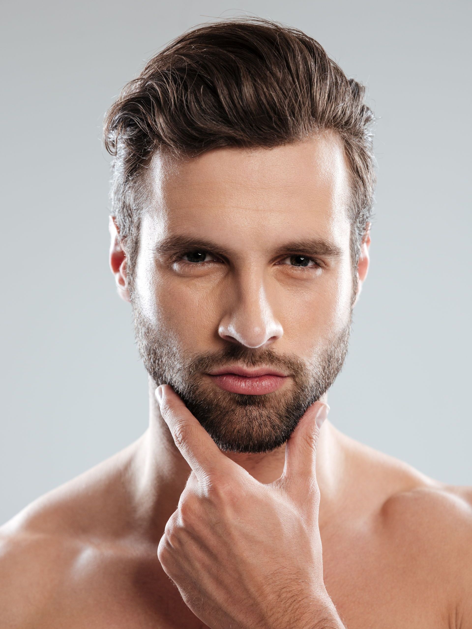 Portrait of a bearded man touching his chin, looking directly at the camera against a light background