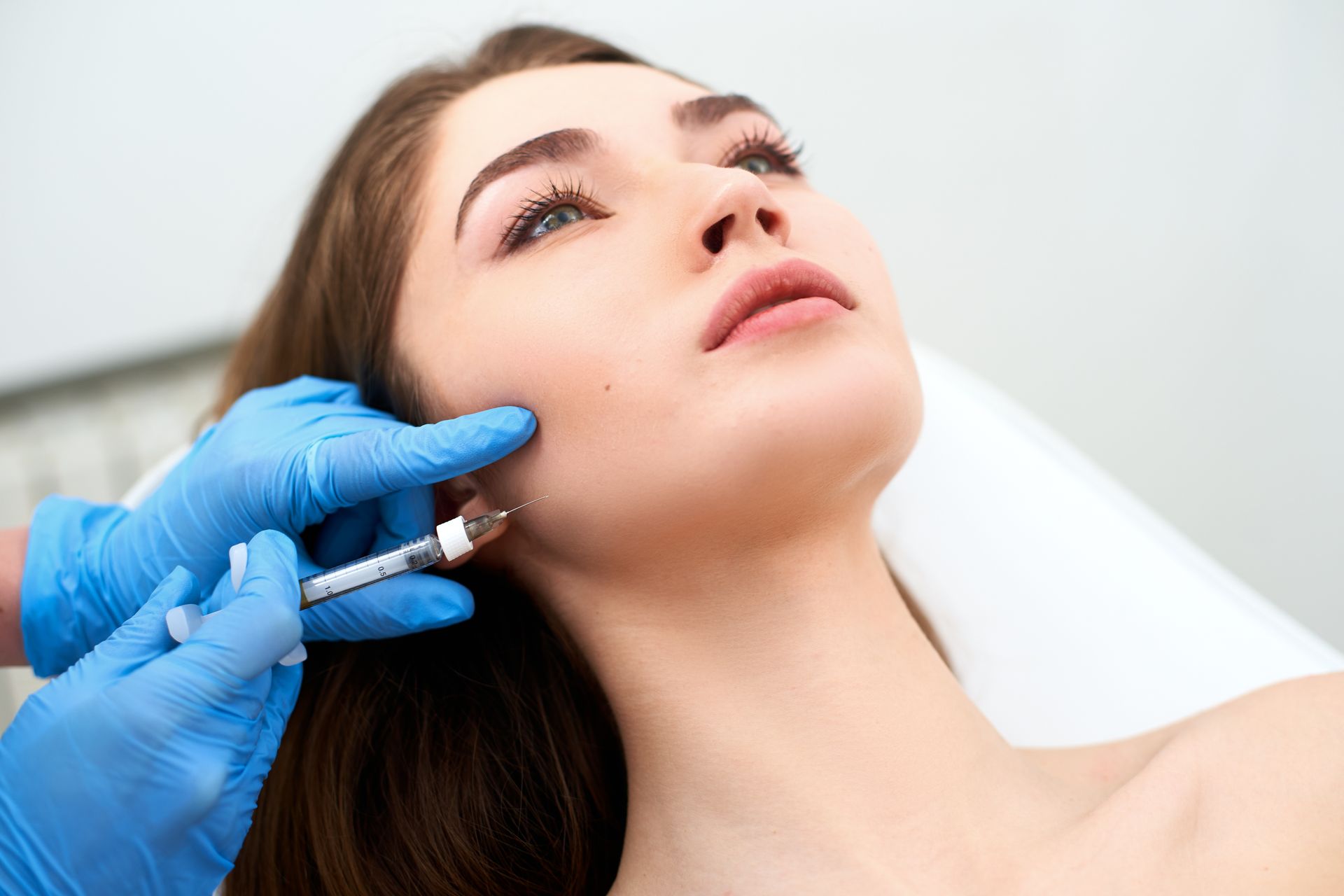 Gloved hand injects a woman’s cheek with a syringe during a cosmetic procedure