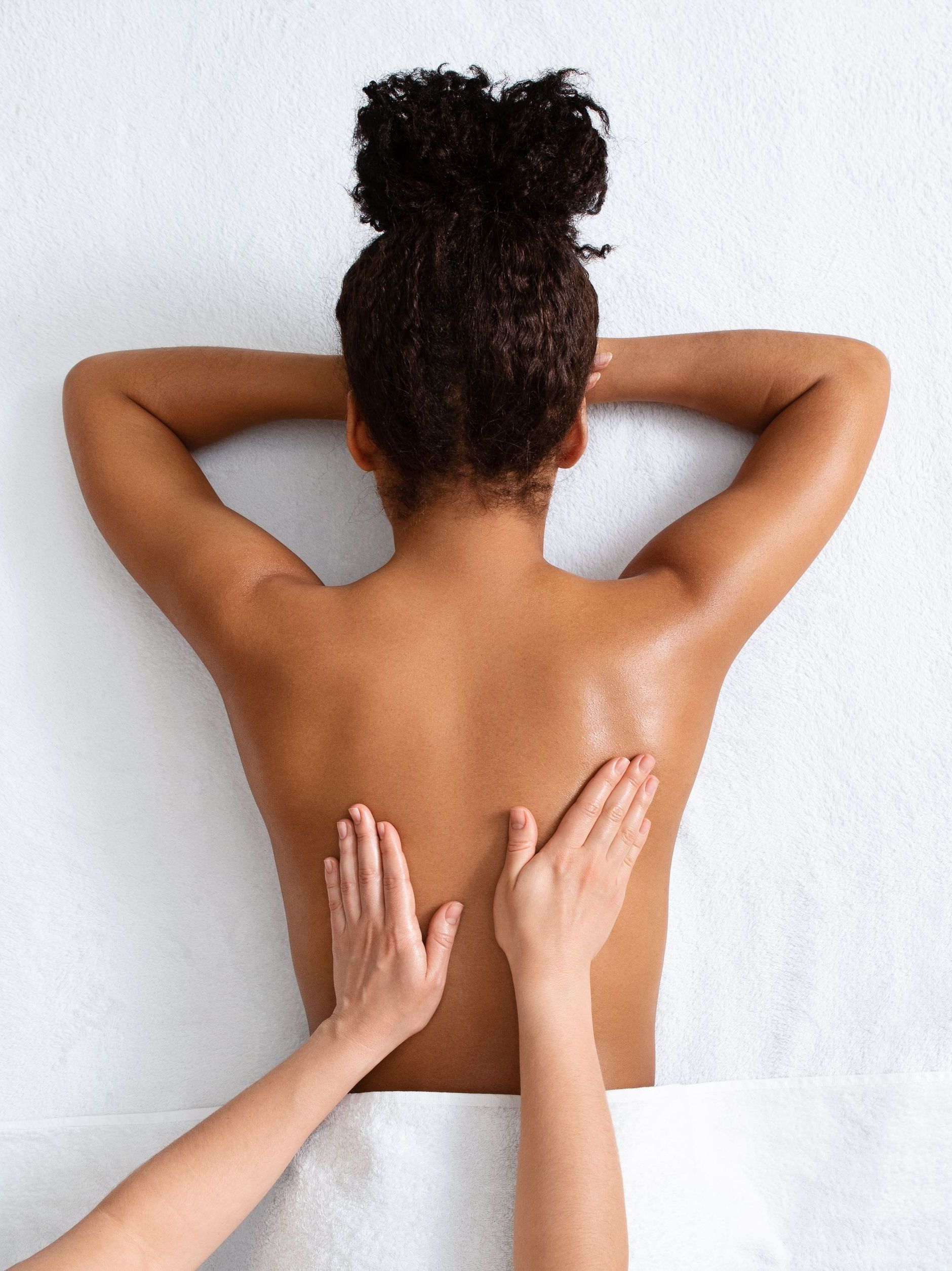 Hands pressing on a person’s bare back and shoulders against a white wall