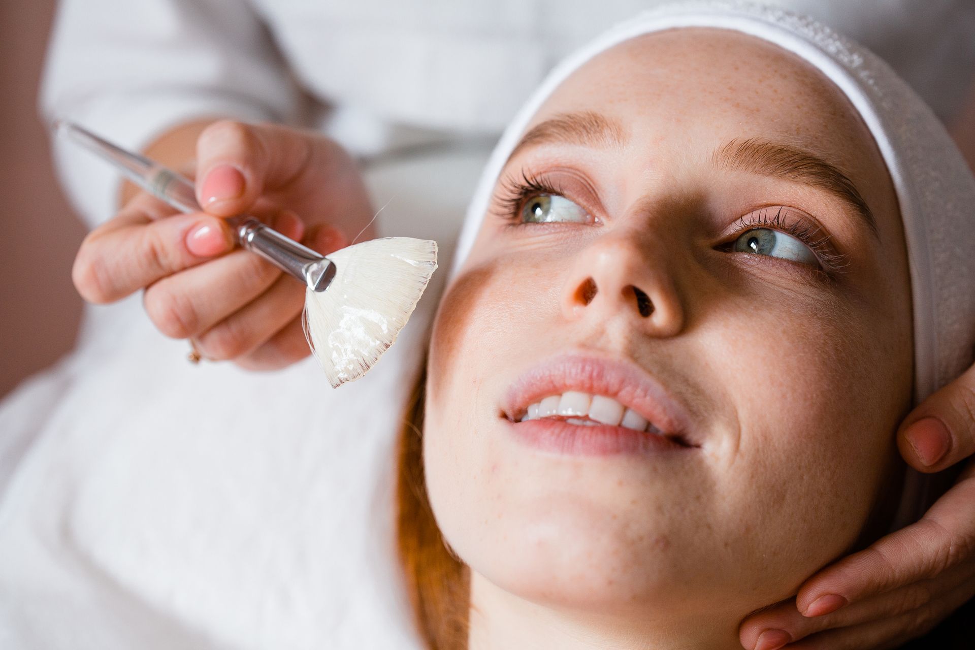 Facial spa treatment with a brush applying cream to a client’s cheek