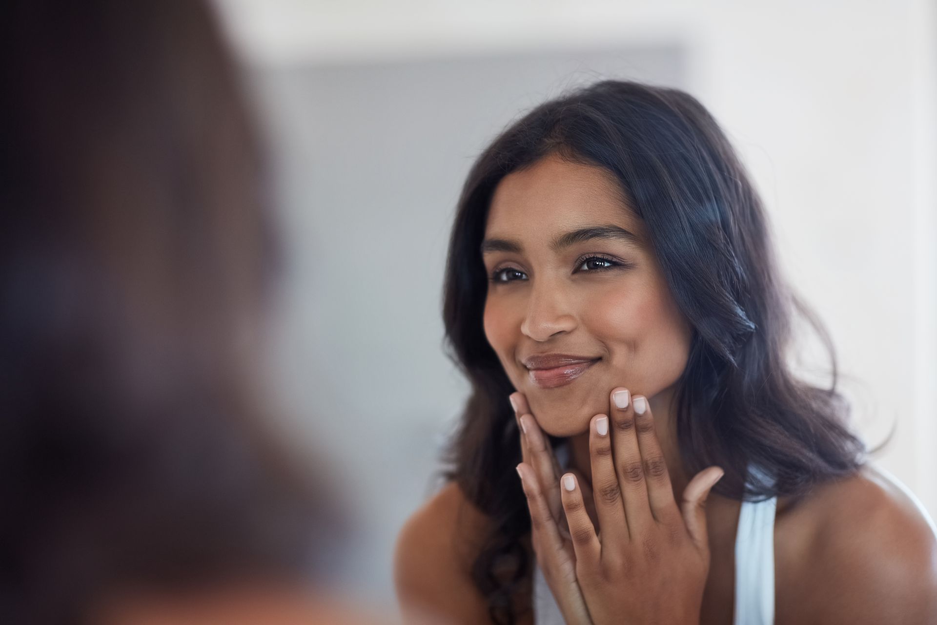 A woman is looking at her face in the mirror.