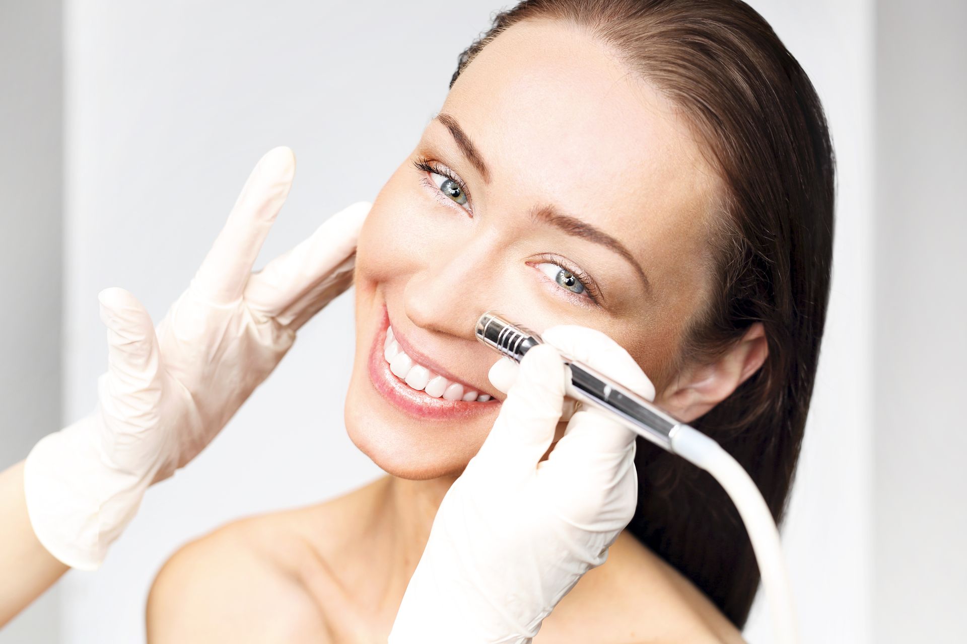 Smiling woman receiving a facial treatment with a handheld device and gloved hands