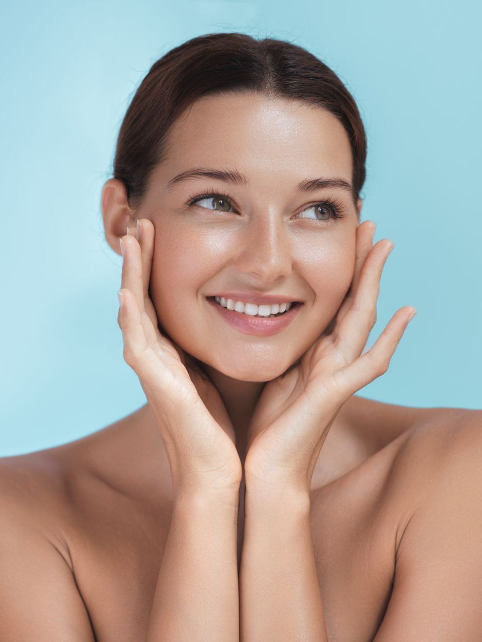 Smiling woman gently touching her face against a light blue background