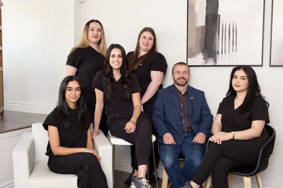 Group portrait of six people in black outfits seated and standing in a bright modern room