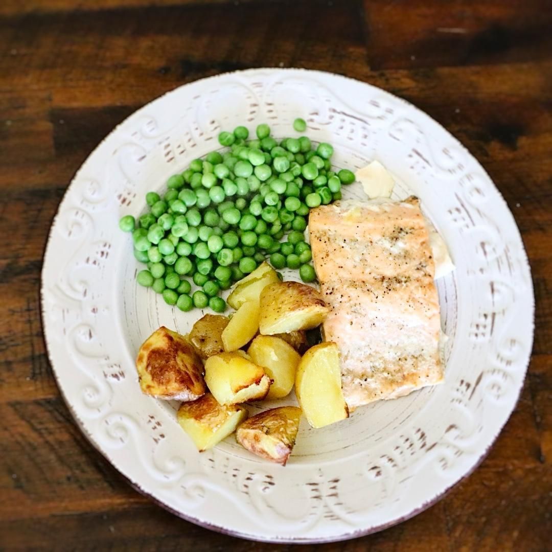 Plate of salmon, peas, and roasted potatoes on a wood table.