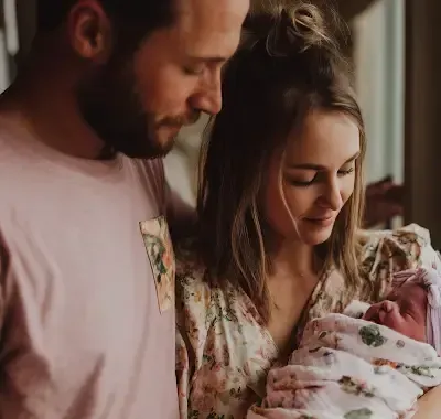 Parents gazing at their newborn baby, wrapped in a floral blanket.