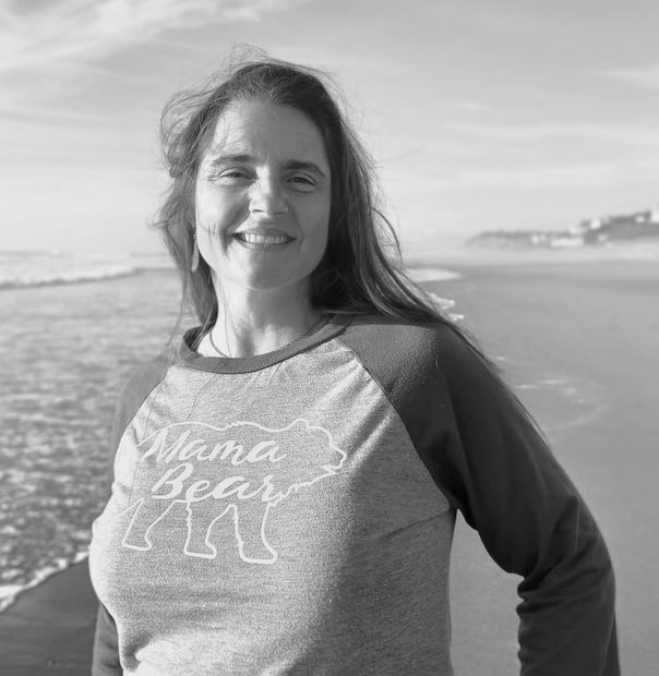 Woman smiling on a beach, wearing a grey