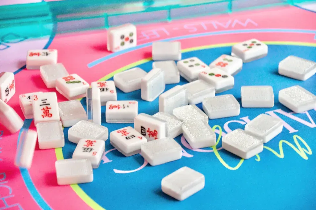 Mahjong tiles scattered on a blue and pink surface, some displaying red and green symbols.