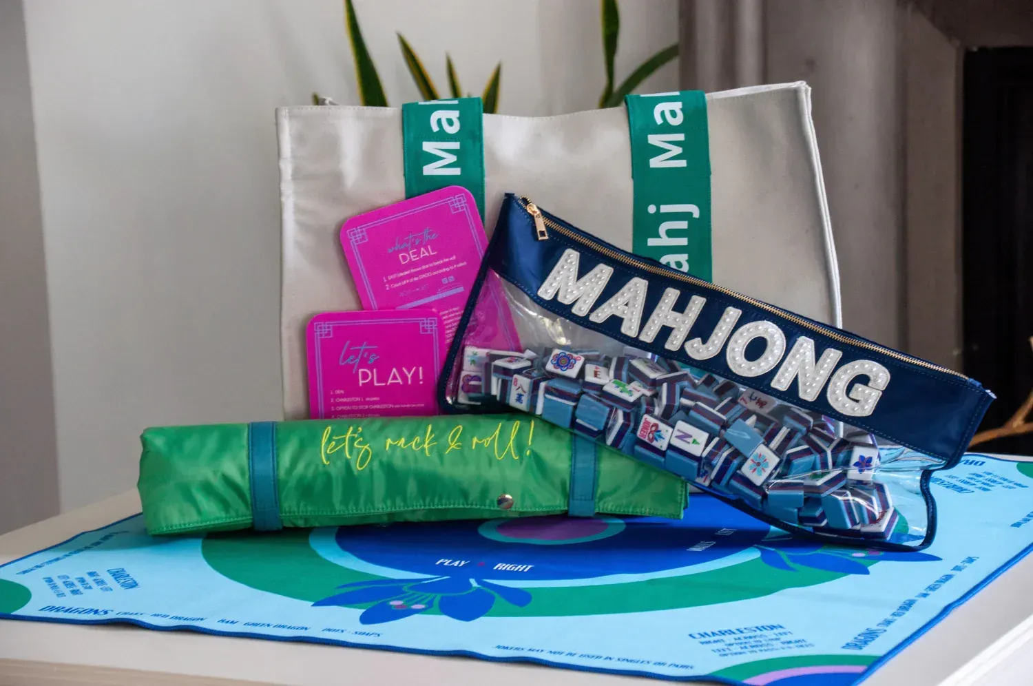 Mahjong set with tote bag, cards, pencil case, and mat on a table. Blue, green, and pink color scheme.