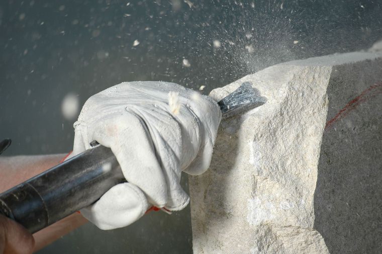 Eine behandschuhte Hand umklammert einen schwarzen Griff auf einer grauen Steinoberfläche, die mit weißem Staub oder Pulver bedeckt ist.