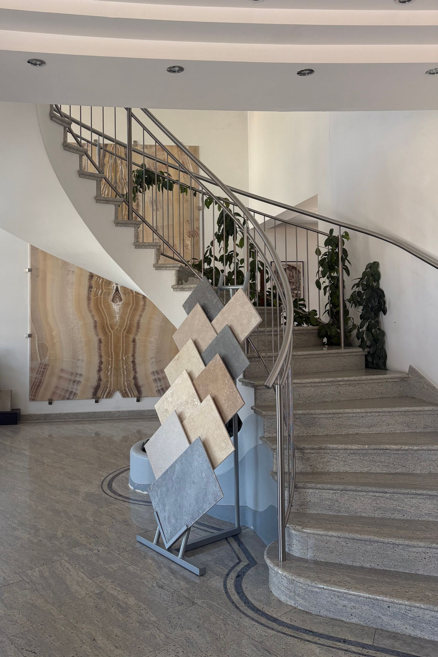 Geschwungene Innentreppe mit dekorativem Metallgeländer, gewebter Wandkunst und Topfpflanzen in einer modernen Lobby