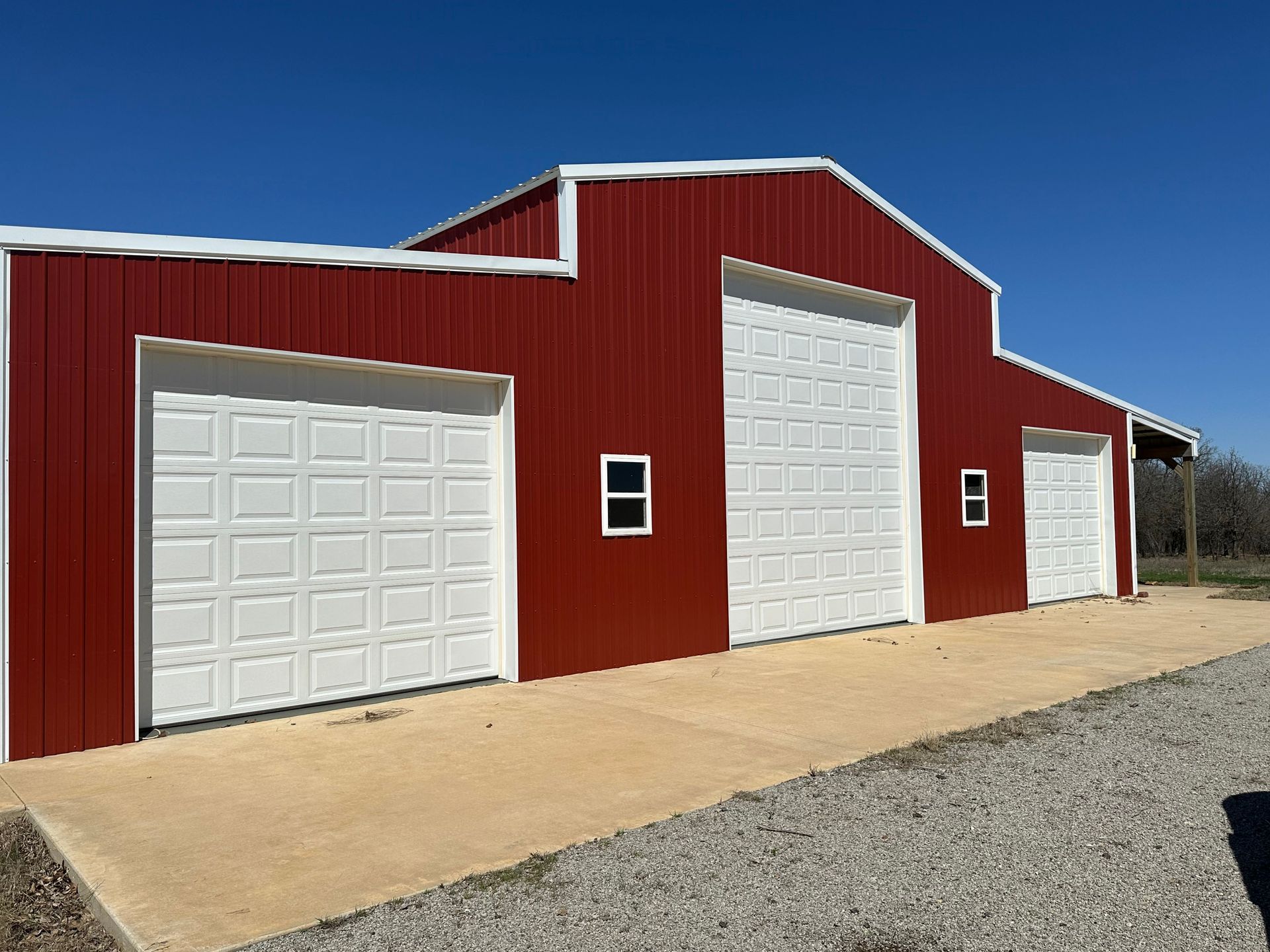 Red barn-style building with white garage doors on a gravel lot by A&C Barn Builders