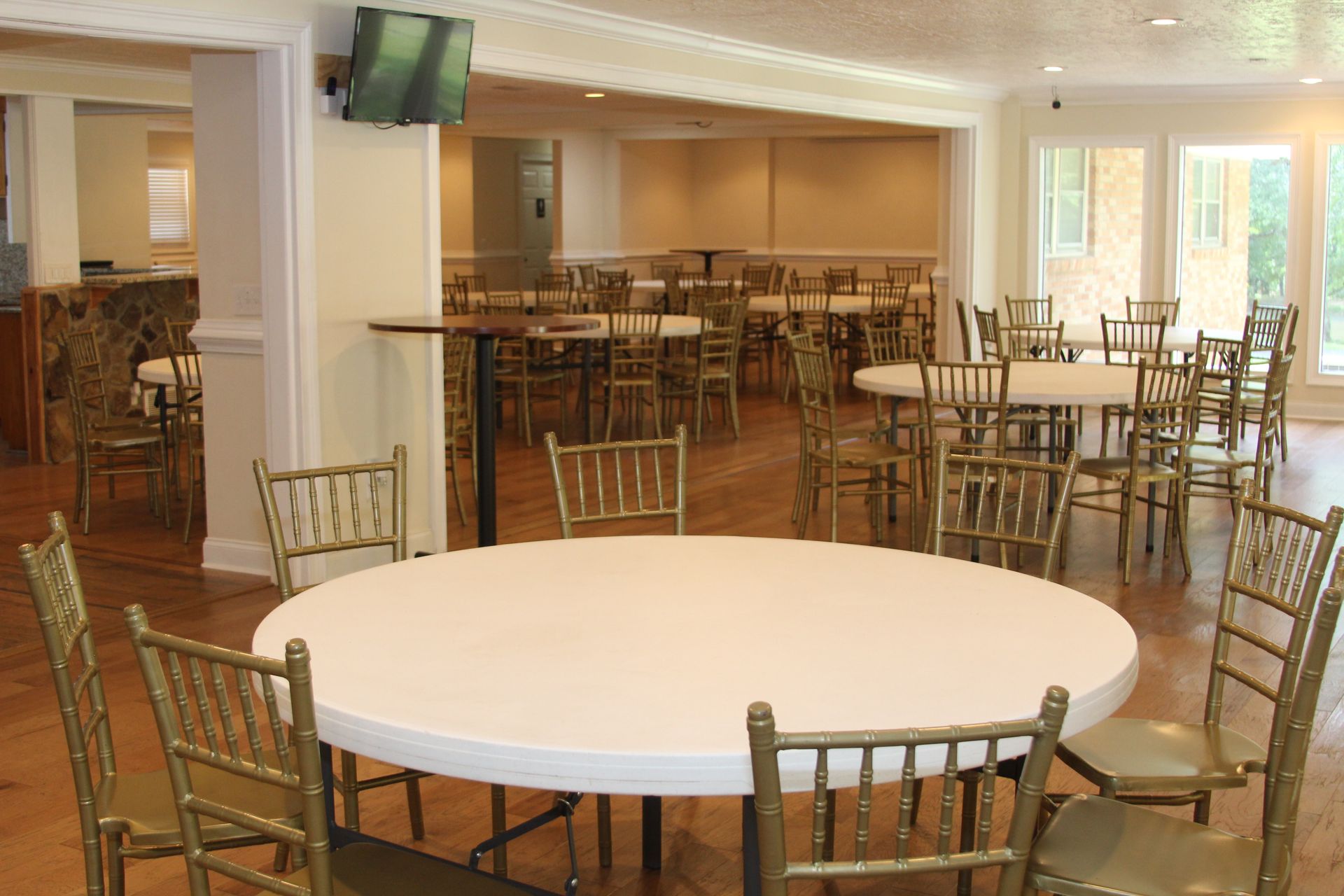 A large room with tables and chairs and a television on the wall.