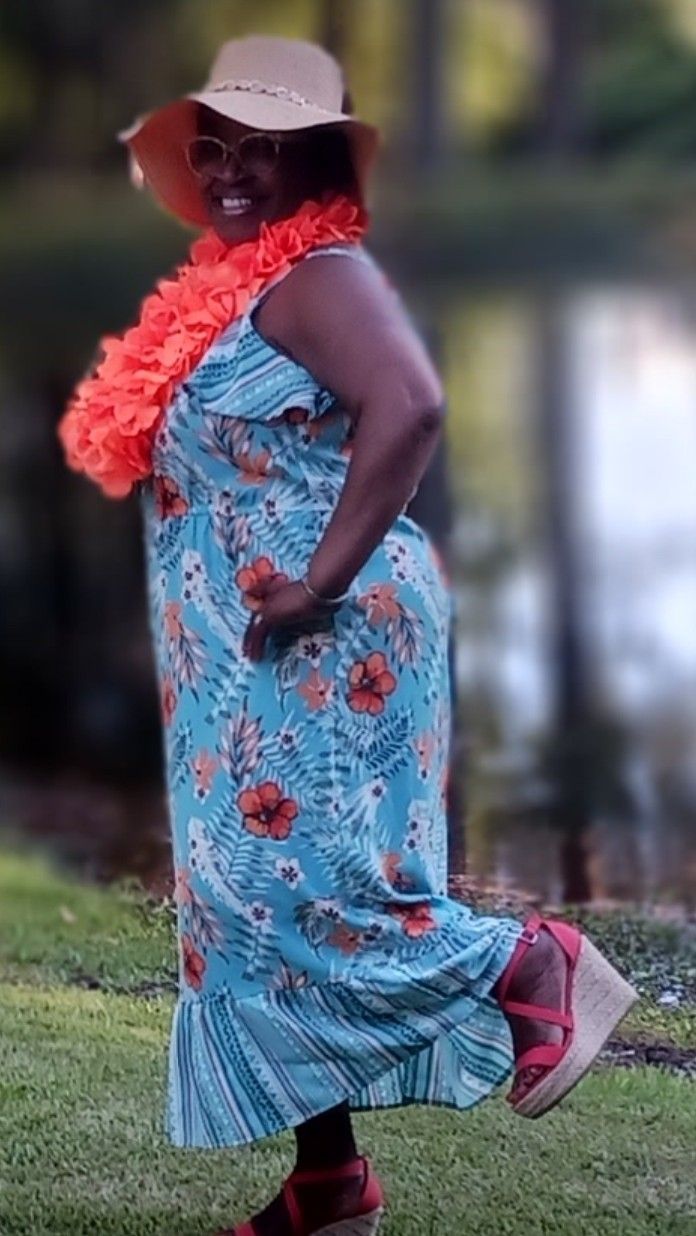 A woman wearing a blue dress and a hat is standing in the grass